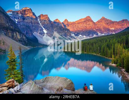 Young Couple enjoying Alpenglow at Moraine Lake during summer in  Banff National Park, Canadian Rockies, Alberta, Canada.  Banff National Park, Albert Stock Photo