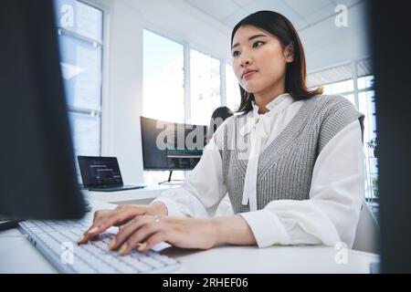 Asian woman, computer and coding in software development or web design at the office. Female person or employee typing on desktop PC in programming Stock Photo