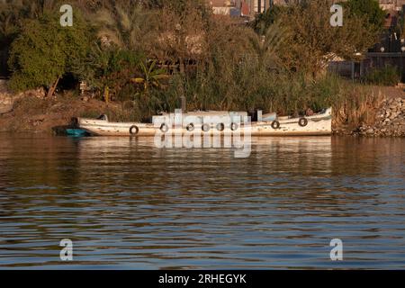 A small wooden riverboat with single funnel moored on the banks of the River Nile, Egypt with reflections Stock Photo