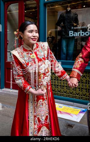 A Chinese Bride Poses For Wedding Photos in Traditional Costume Outside The Barbour Luxury Clothes Shop In Leadenhall Market, London, UK. Stock Photo