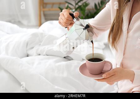 Woman pouring espresso from geyser coffee maker into cup in bed Stock Photo