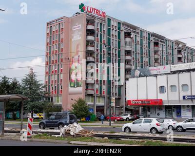 Run down apartment block with advertising boarding on side, traffic and tram stop in front. Sarajevo, Bosnia and Herzegovina, August 16,2023. Stock Photo