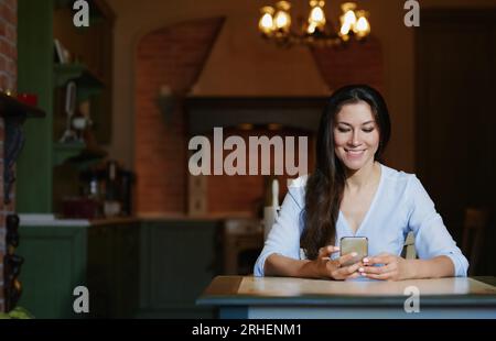 Smiling woman sitting and table and using smartphone Stock Photo