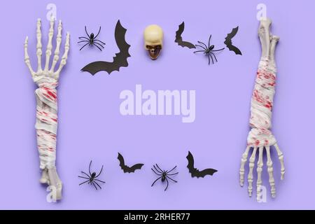 Frame made of skeleton hands, skull, paper bats and spiders for Halloween celebration on purple background Stock Photo