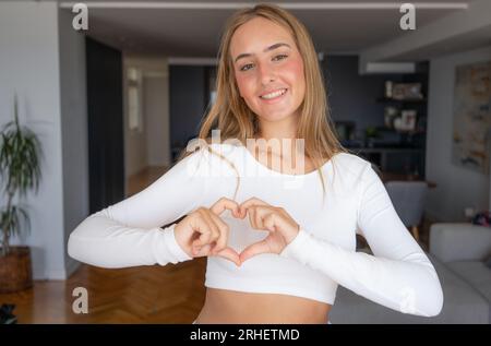 Young woman making heart with hands indoors. Volunteer concept Stock Photo
