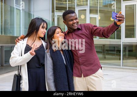 Happy coworkers taking a selfie photo at work break. Group of young friends smiling at office outdoors. Ethnic diversity. Stock Photo