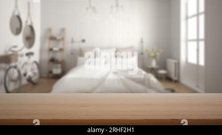 Empty wooden table, desk or shelf with blurred view of scandinavian white bedroom, bed with pillows, bicycle, decors and mirror, modern interior desig Stock Photo