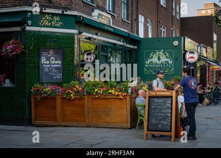 London, UK: The Windmill pub on The Cut in Lambeth, London. People sit and stand outside the pub. Stock Photo