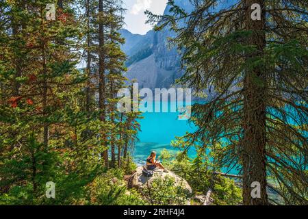 Woman reading a book in the Forest, Moraine Lake during summer in  Banff National Park, Canadian Rockies, Alberta, Canada.  Banff National Park, Alber Stock Photo