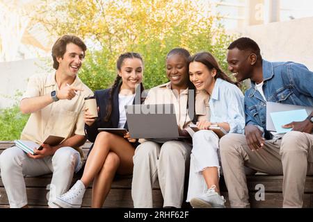 Multiracial group of students sitting on bench, using laptop Stock Photo