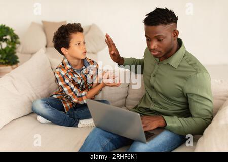 African American Dad Ignoring His Son Using Laptop At Home Stock Photo