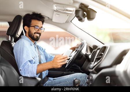 Happy young indian guy using smartphone while driving car Stock Photo
