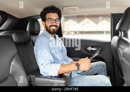 Handsome indian businessman sitting in car taxi, using digital tablet Stock Photo