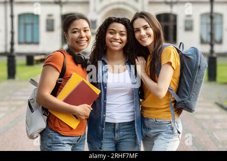 Three Happy Female Students With Backpack And Workbooks Posing Together Outdoors Stock Photo
