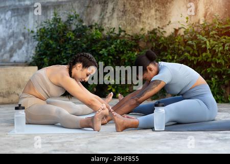 Calm millennial black and caucasian women doing body stretching, practicing yoga together on mat with bottles Stock Photo