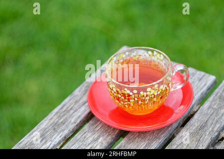 Glass cup of tea on a wooden rustic table and green grass on the background. Stock Photo