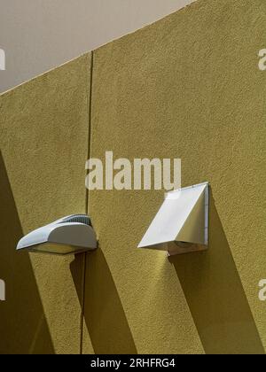 Lamp and matching vent port with shadows on golden stucco covered wall Stock Photo