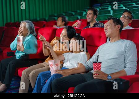 Happy Asian family of father, mother, son, and grandmother cherishes weekend moments at the cinema, sharing joy and togetherness while watching a movi Stock Photo