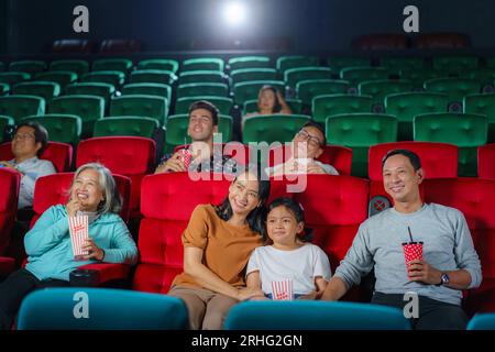 Happy Asian family of father, mother, son, and grandmother cherishes weekend moments at the cinema, sharing joy and togetherness while watching a movi Stock Photo