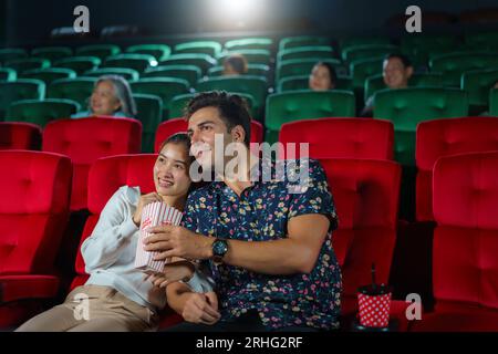 Couples enjoy movies while holding popcorn, creating a cozy and entertaining movie night experience at the cinema. Stock Photo