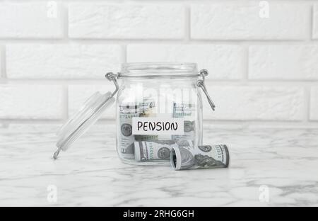 Glass jar with word Pension and banknotes on white marble table Stock Photo