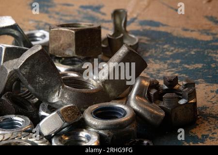 Industrial allure: A pile of metal nuts on an old workbench, accentuated by a smear of blue paint. Perfect for DIY, construction, or mechanical themes Stock Photo