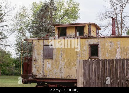 Exterior view of a deteriorating yellow 19th century railway train caboose car with weathered wood siding. Stock Photo