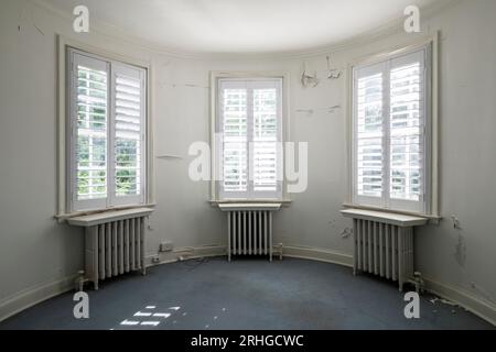 A trio of windows inside of a room that has a curved wall inside of an abandoned house. Stock Photo