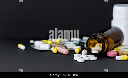 Pill bottle with spilling varied medicine over black. Stock Photo