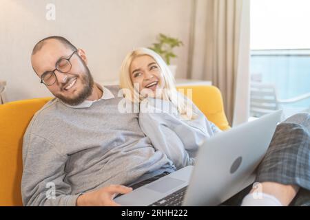 Happy young couple laughing and having fun at home, making online purchases in internet stores. Stock Photo