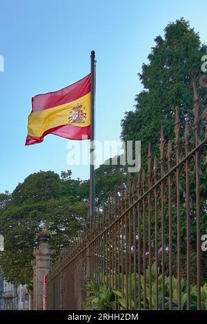 Spanish flag blowing in the wind on a mast on a metal fence. Stock Photo