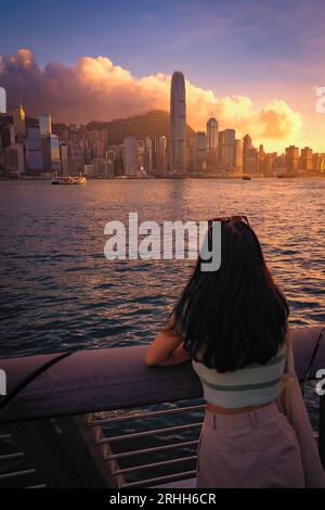 Scenic, awesome view of a tourist looking at Victoria Harbour and Hong Kong's fantastic skyline, against a dramatic sunset and sky, Hong Kong, China Stock Photo