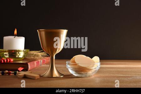 Cup of wine and hosts on wooden table with bible and candle for eucharist black isolated background. Front view. Stock Photo