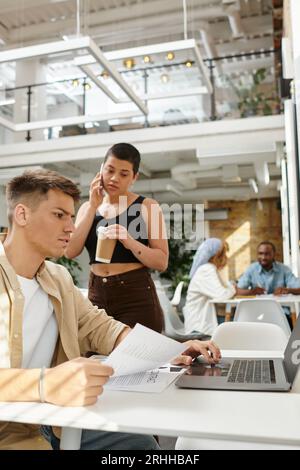 focused man using laptop, woman with tattoo having phone call, startup, coworking, busy, business Stock Photo
