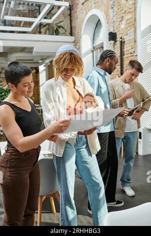 interracial office workers smiling, looking at project on papers, coworking, startup, generation z Stock Photo