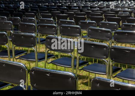 Rows of empty black chairs on grass field Stock Photo