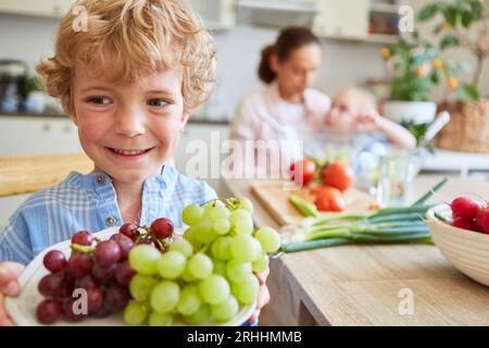 Smiling blond boy looking away while holding grapes in plate home Stock Photo