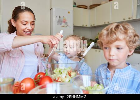 Smiling mother preparing salad with son and daughter in kitchen at home Stock Photo