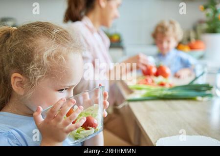 Blond girl smelling bowl of vegetables while preparing food in kitchen at home Stock Photo