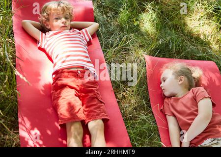 High angle view of siblings relaxing on yoga mat at park Stock Photo