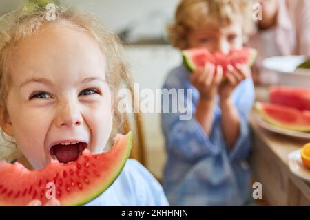 Blond girl screaming while looking away holding watermelon slice at home Stock Photo