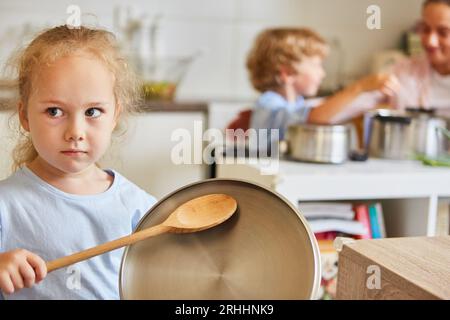 Serious girl looking away while holding wooden ladle and lid at home Stock Photo