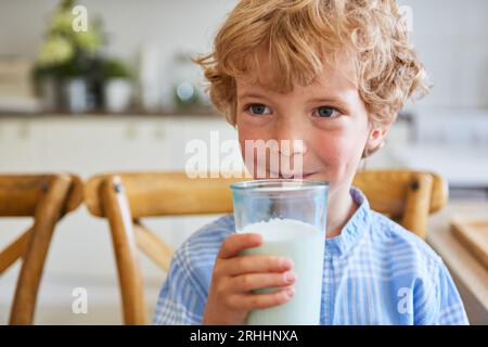 Thoughtful blond boy holding glass of milk sitting at home Stock Photo