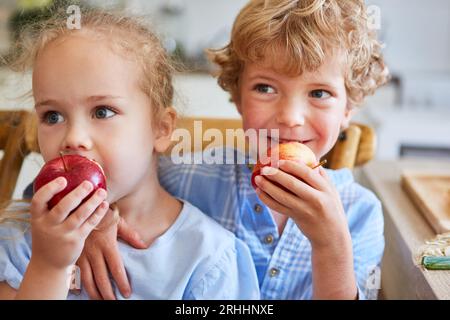 Brother and sister eating fresh apples sitting at home Stock Photo