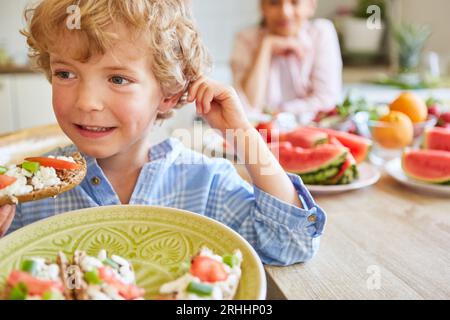 Smiling blond boy looking away while eating bruschetta in kitchen at home Stock Photo