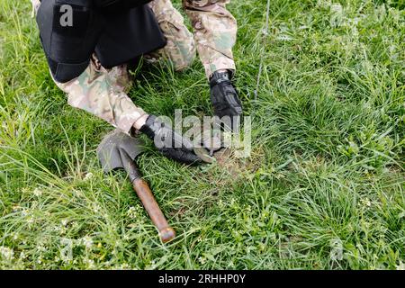 A man in a military uniform and a bulletproof vest works in the forest to demine the territory. A man defuses an anti-personnel mine. Stock Photo