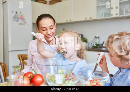 Daughter eating vegetable salad using spork with mother and brother in kitchen at home Stock Photo