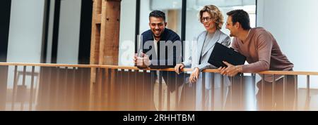 Creative design team stands on an interior balcony discussing ideas. Two business men and one business woman talk about their next project. Group of p Stock Photo