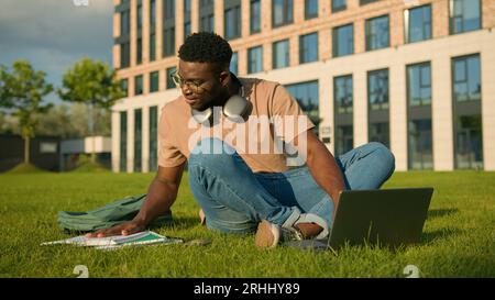 Happy smiling African American man university college academy student guy teenager male studying homework online on grass meadow in park study Stock Photo