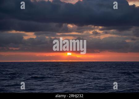 Colorful red and orange sunset with dark blue sky in the deep blue ocean, sea. Stock Photo